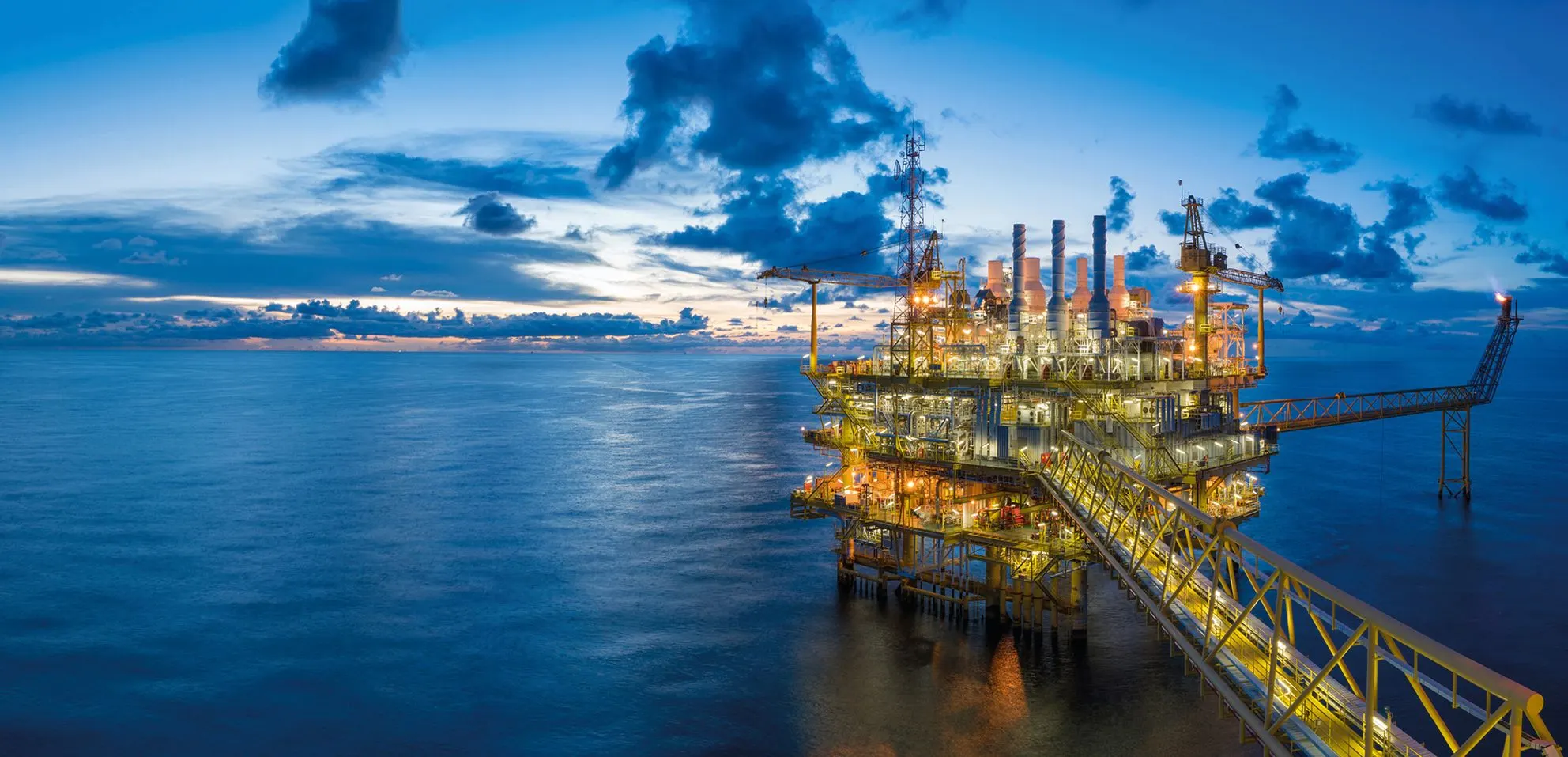 Offshore oil platform lit up at dusk over a calm sea