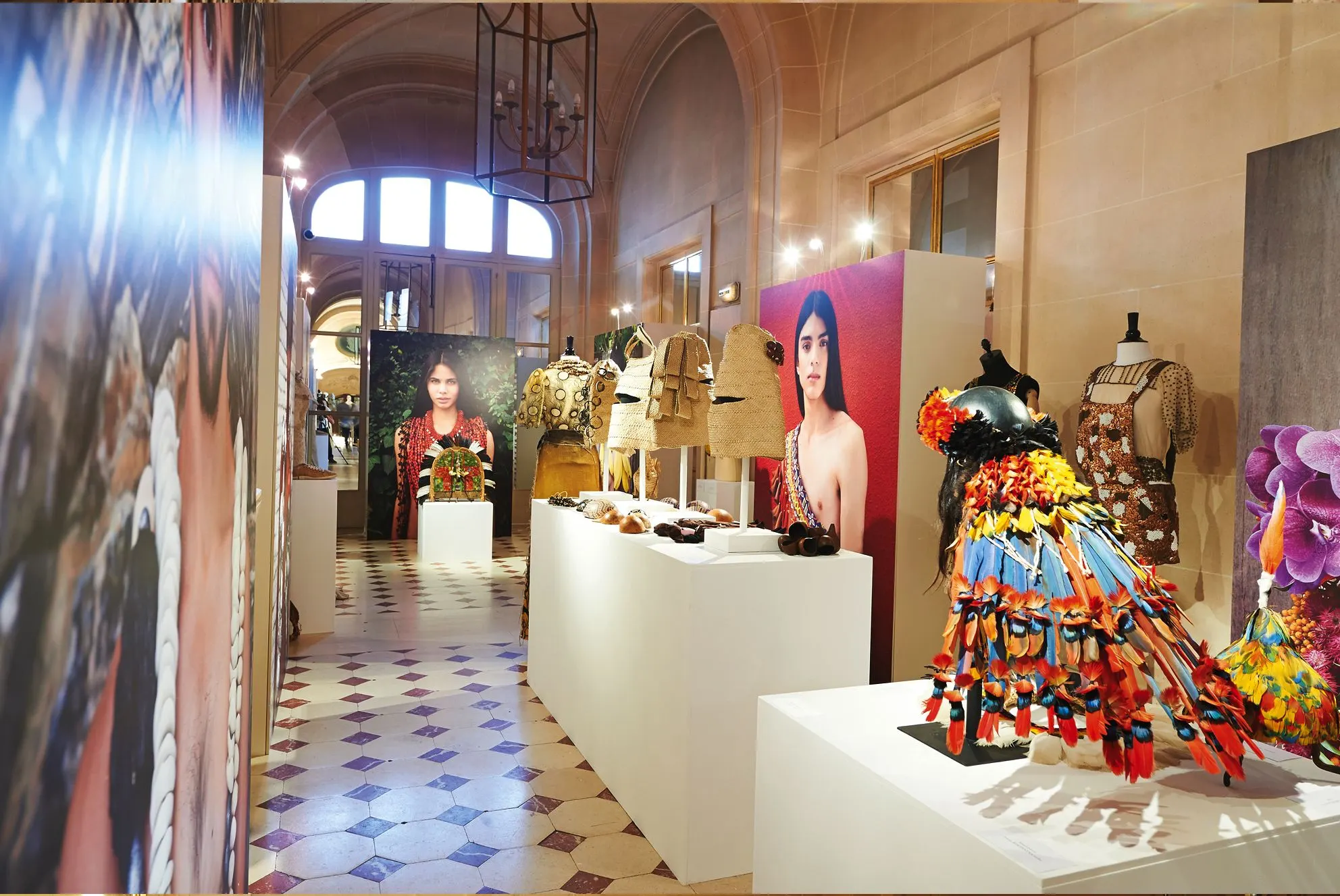 Exhibition gallery with mannequins in colourful feathered costumes and large portraits on the walls