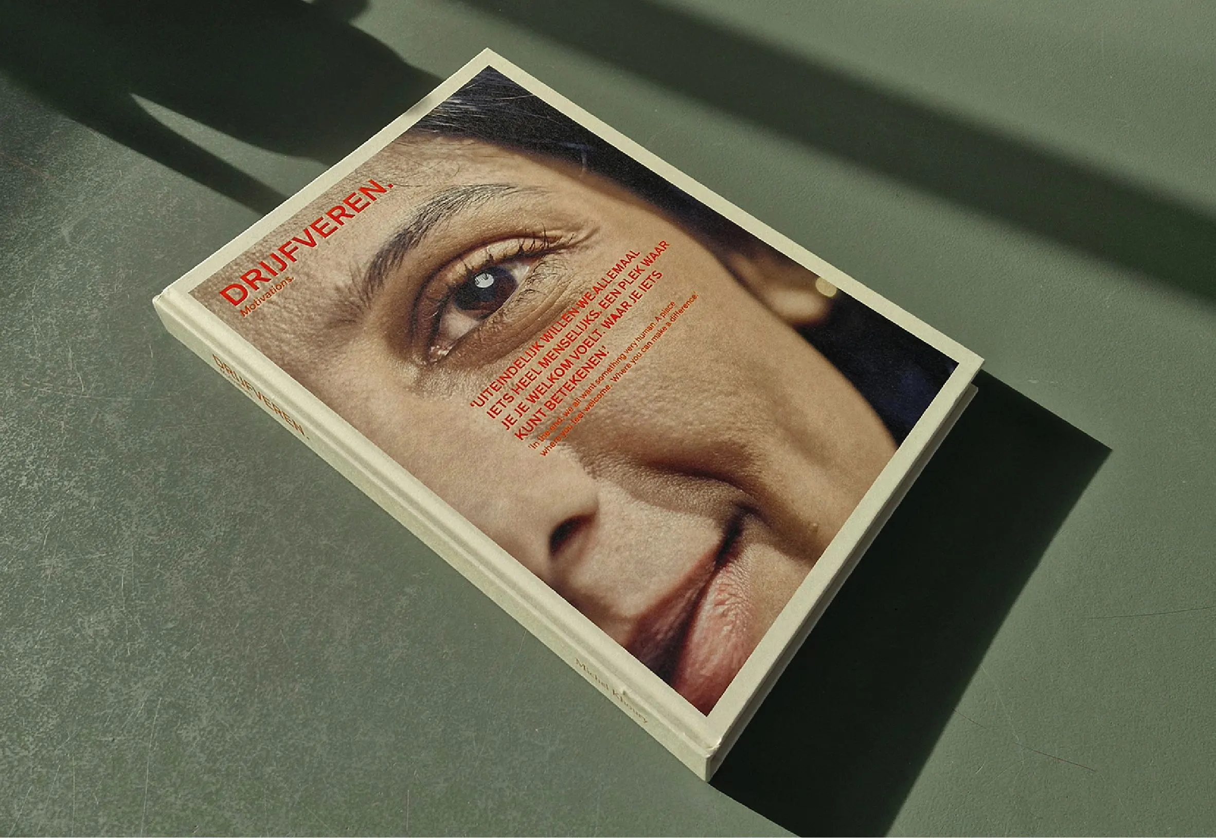Drijfveren publication lying on a green surface, its cover a close-up of a woman's eye and face with red title text