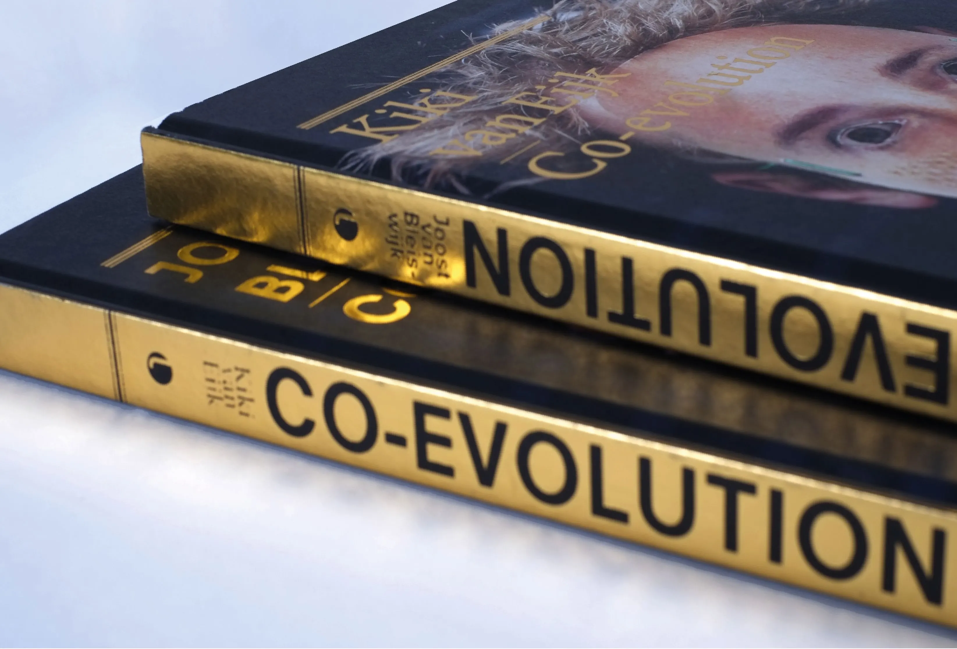 Spines of two Co-evolution books in black with gold lettering, with a face on the covers