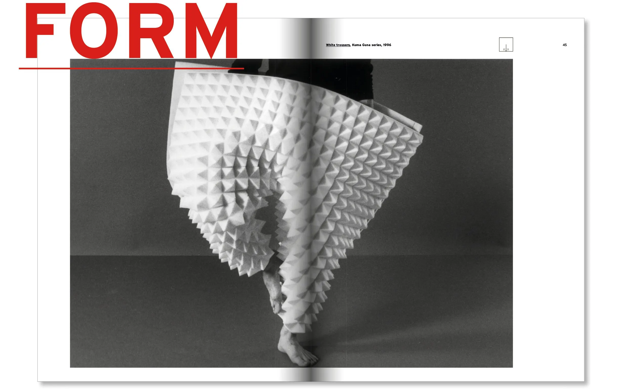 Book spread with a black and white photo of a figure in a white pleated, spiky sculptural garment and red letters