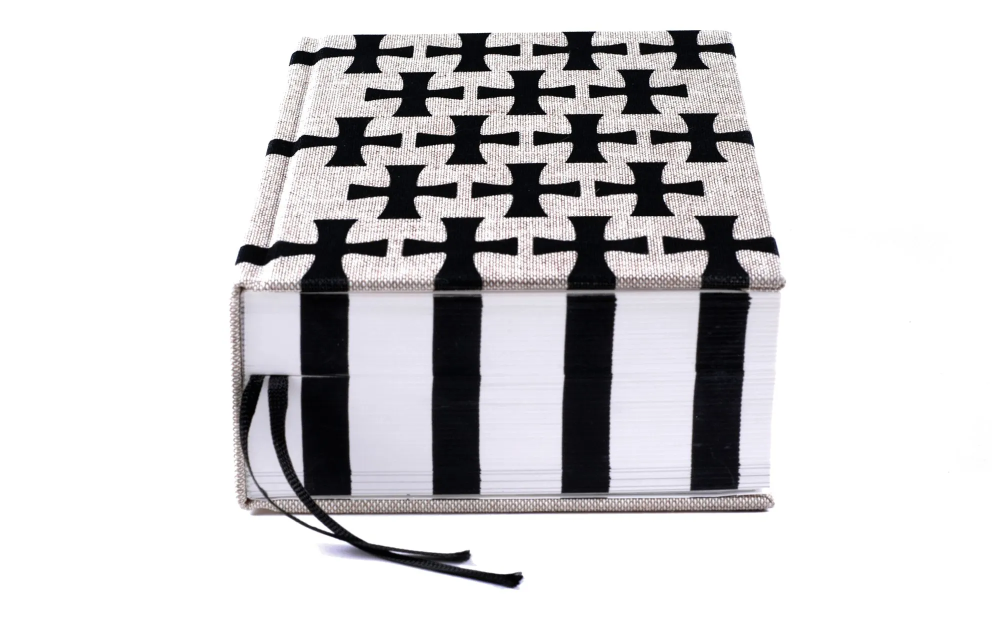 Thick book with a white-and-black cross-pattern fabric cover, black ribbon bookmarks and striped page edges