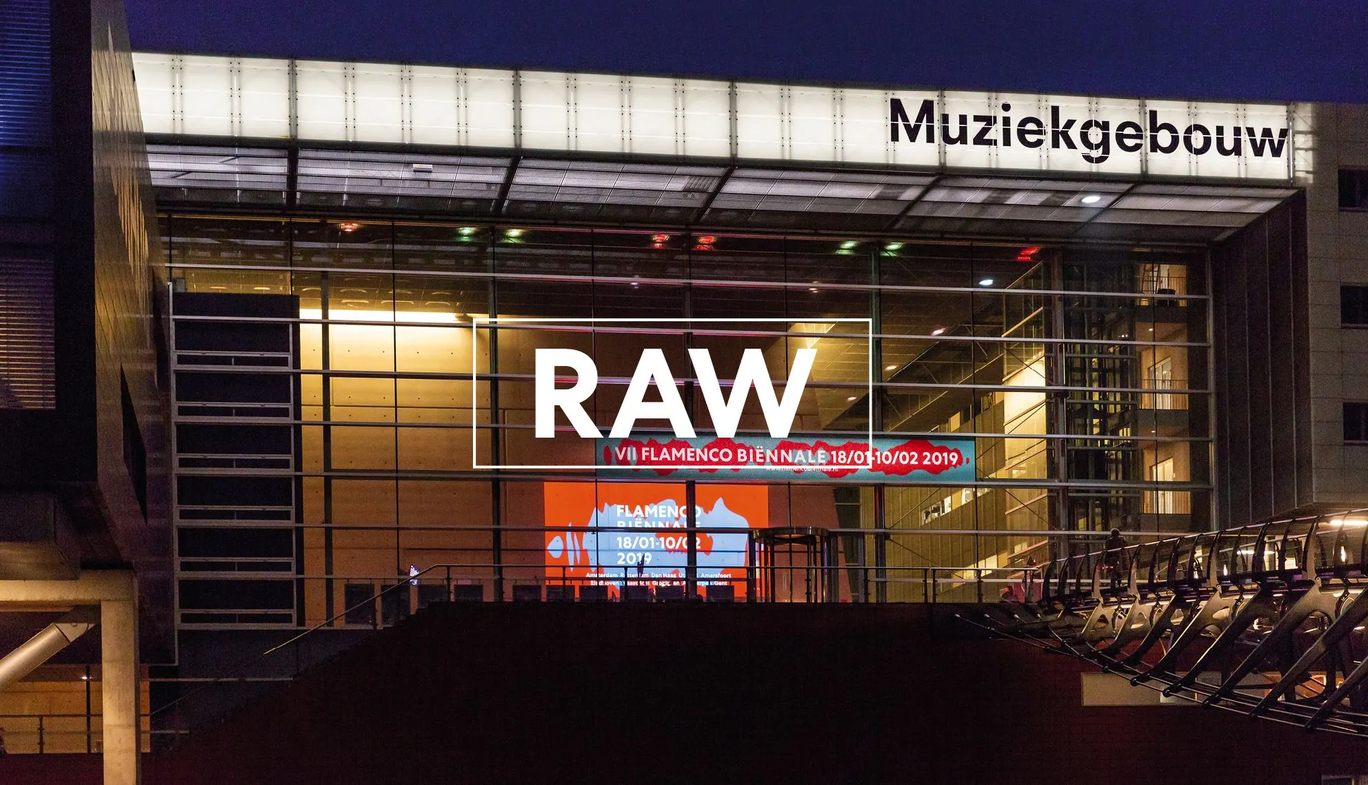 Muziekgebouw glass facade at night with Flamenco Biënnale signage and the word Raw