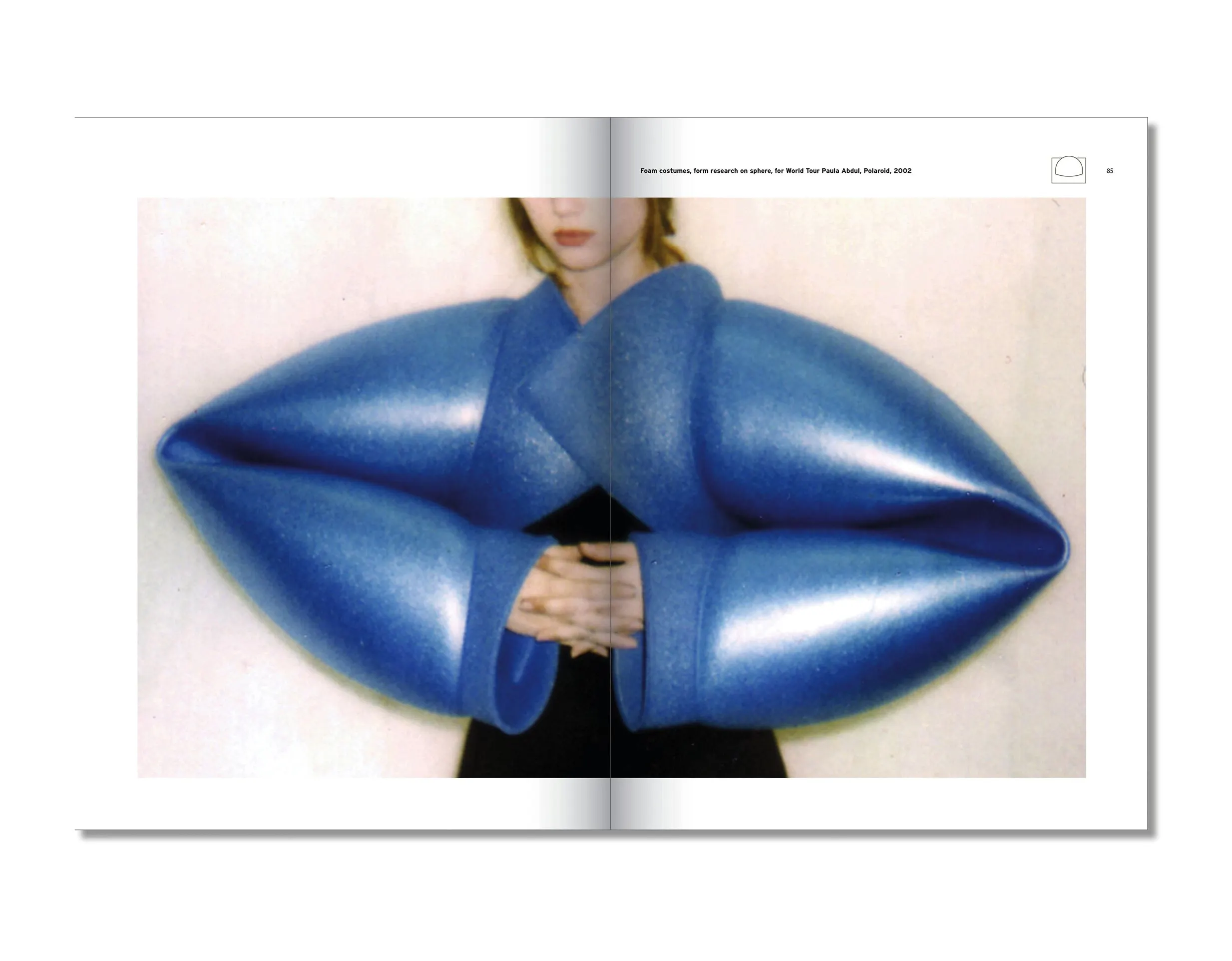 Book spread with a photo of a person wearing a large blue inflated sculptural garment shaped like lips
