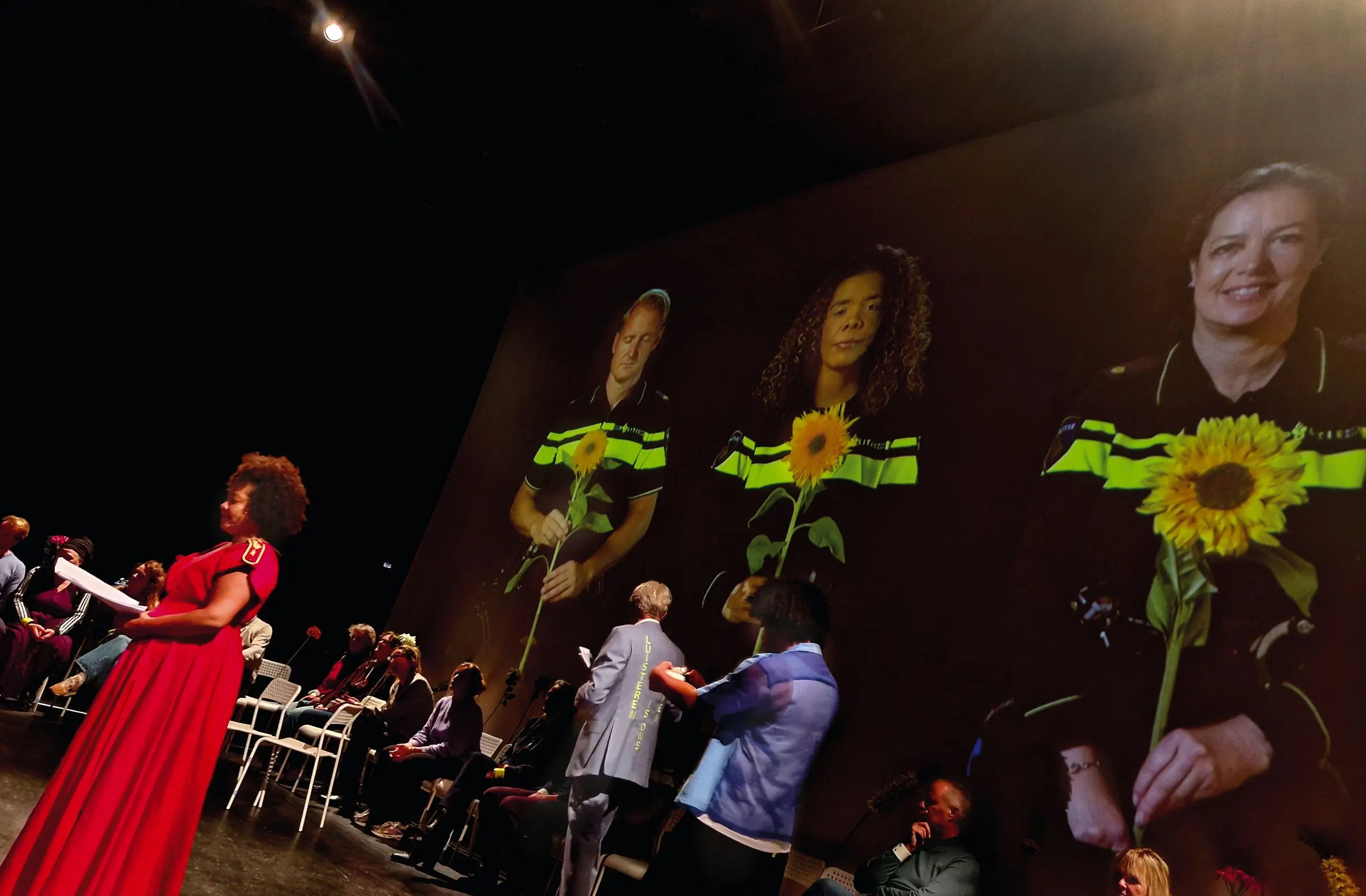 Theatre performance with a singer in a red dress and projected portraits of police officers holding sunflowers