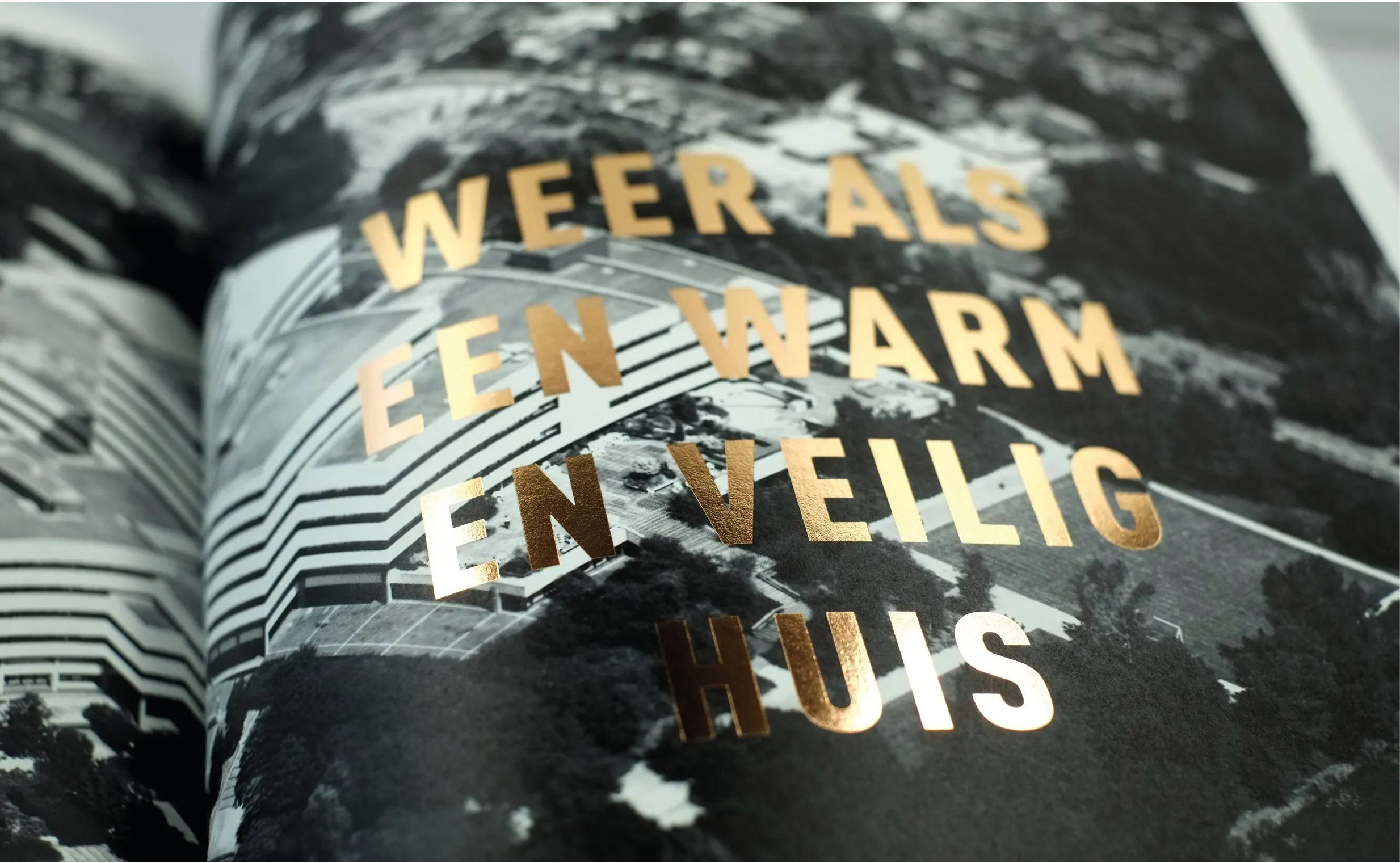 Book spread in gold foil on a black-and-white building photo reading Weer als een warm en veilig huis