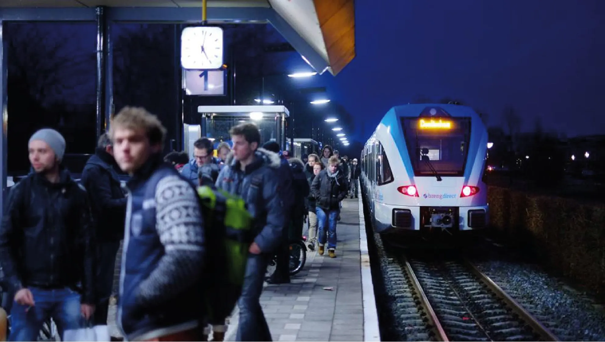 Commuters on a station platform at night as an Arriva train arrives under the lights