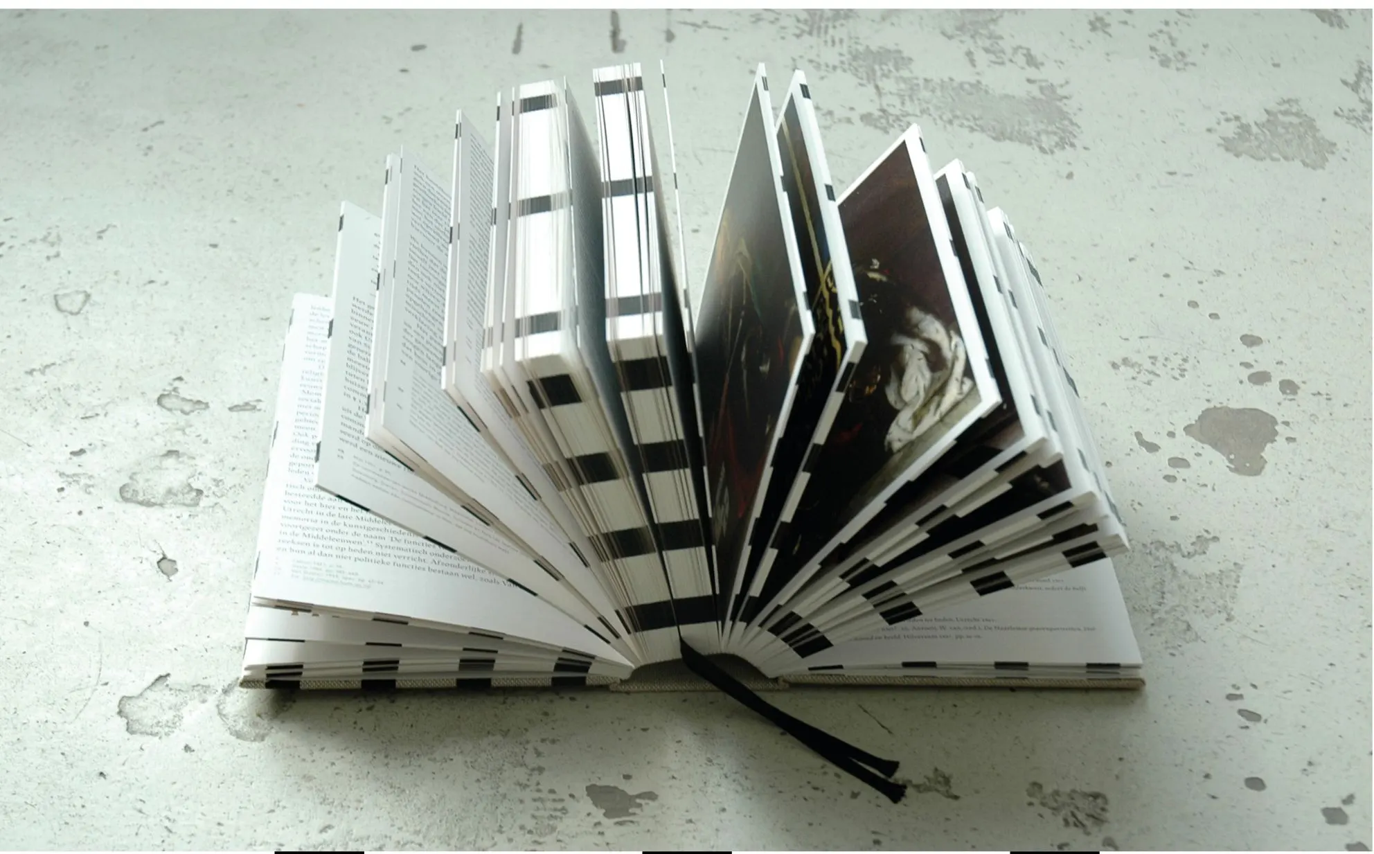 Book fanned open on a weathered surface, showing striped page edges and portrait pages with a black ribbon