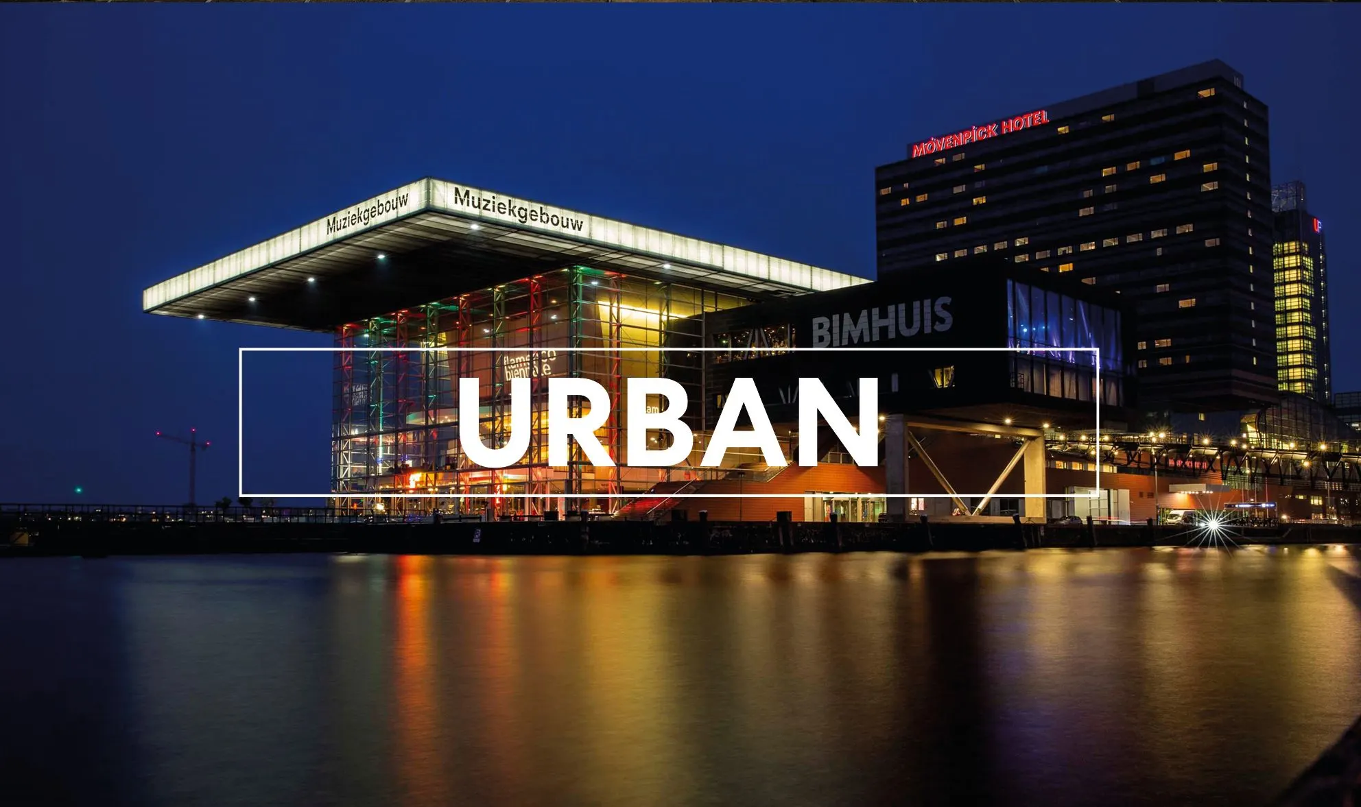 Muziekgebouw illuminated at dusk beside the water with the word Urban