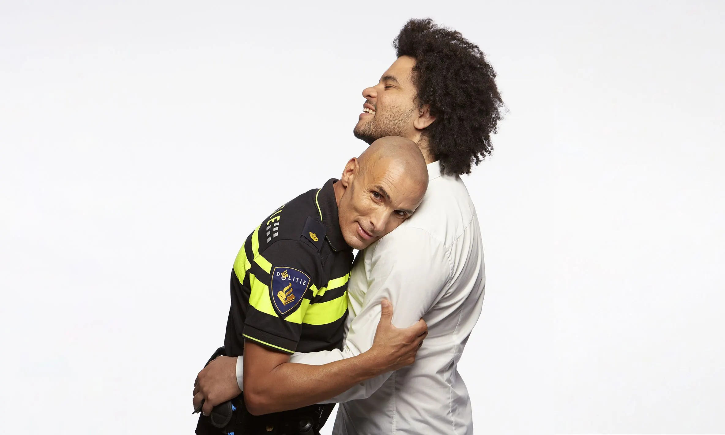 Police officer in uniform and a man in white shirt embracing, laughing, against a white background