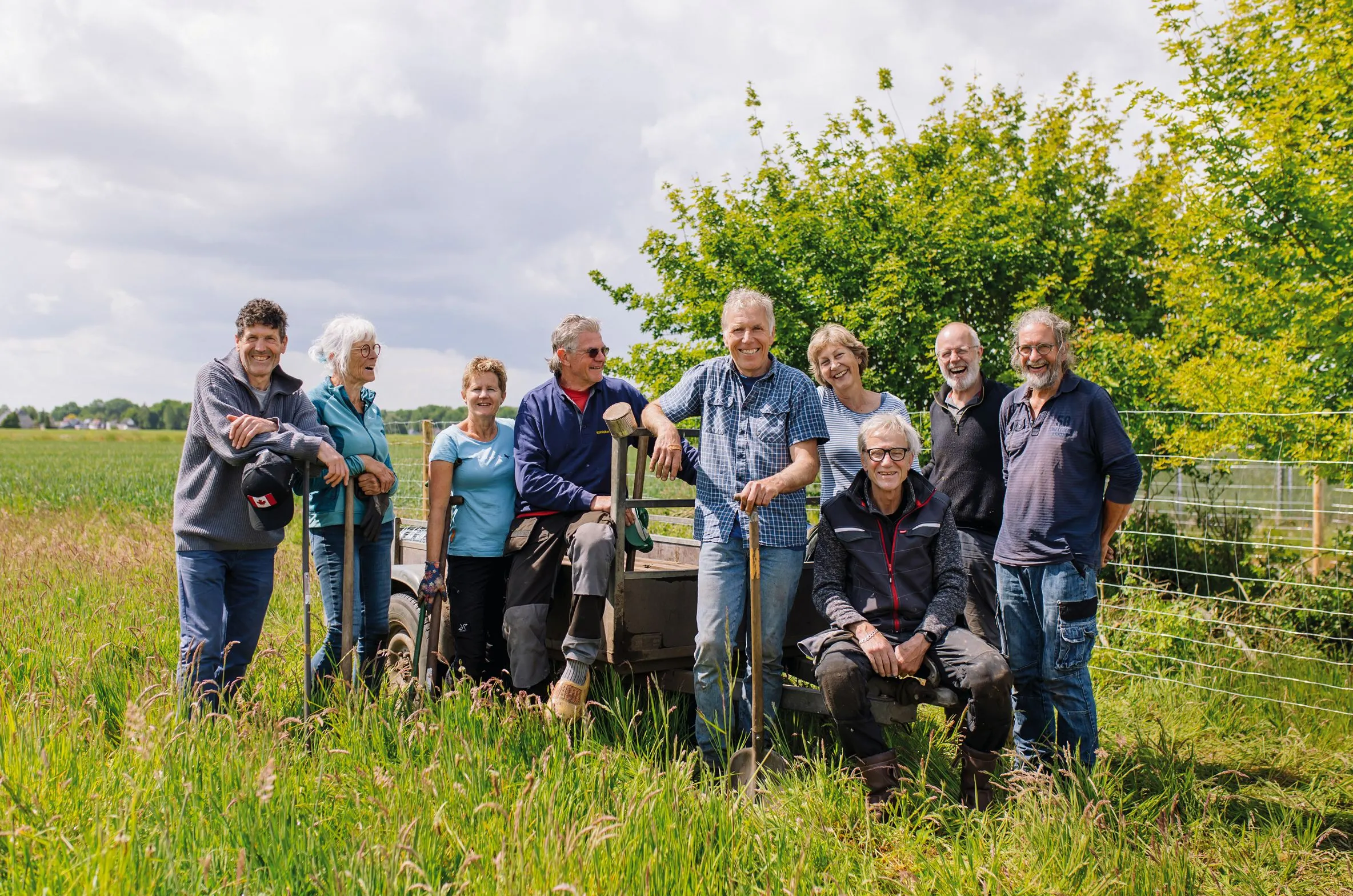 Group portrait of about ten smiling people standing together in a green field with trees behind