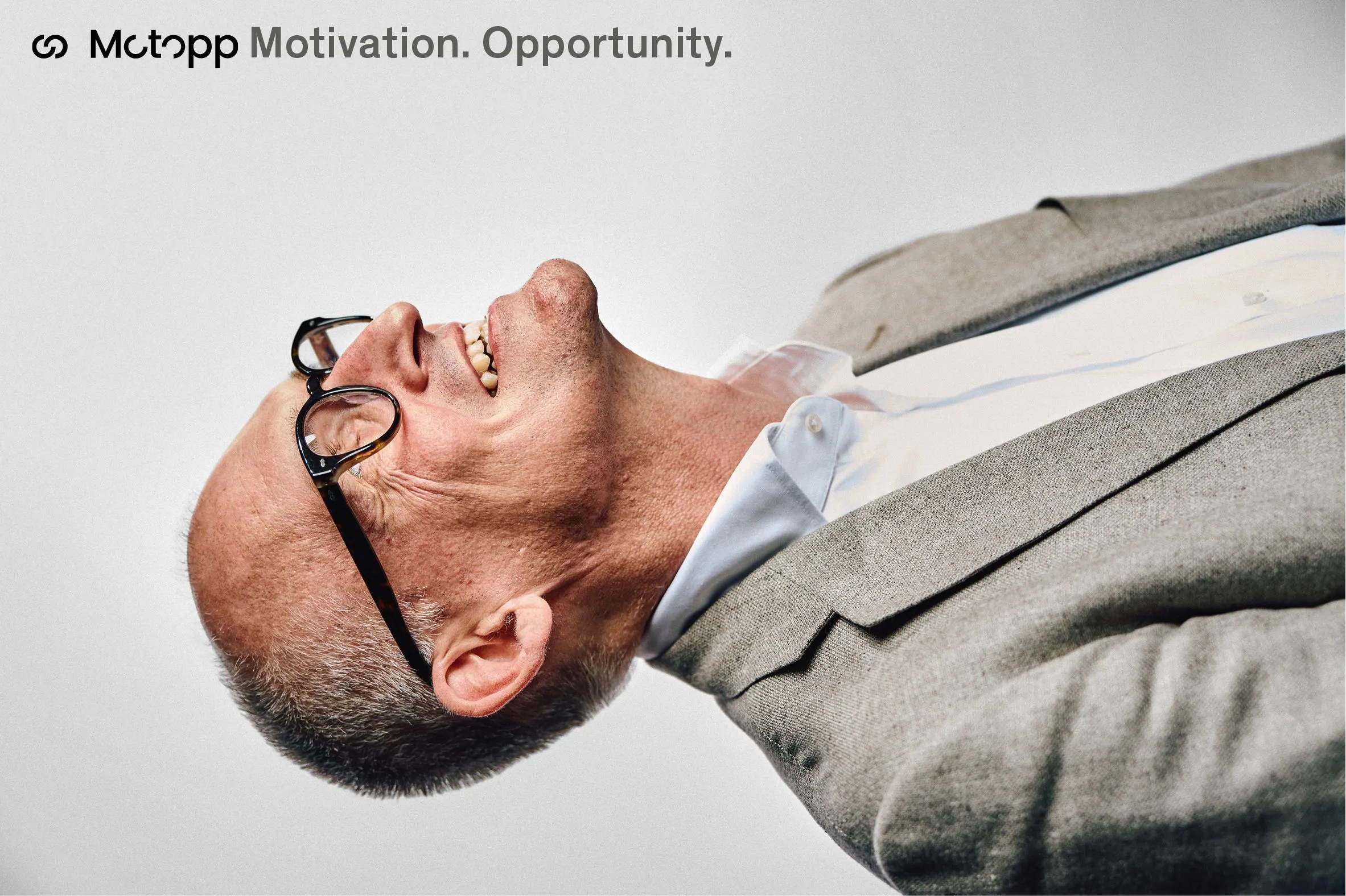 Portrait of a laughing man with glasses in a grey jacket, rotated sideways, with the Motopp 'Motivation. Opportunity.' tagline