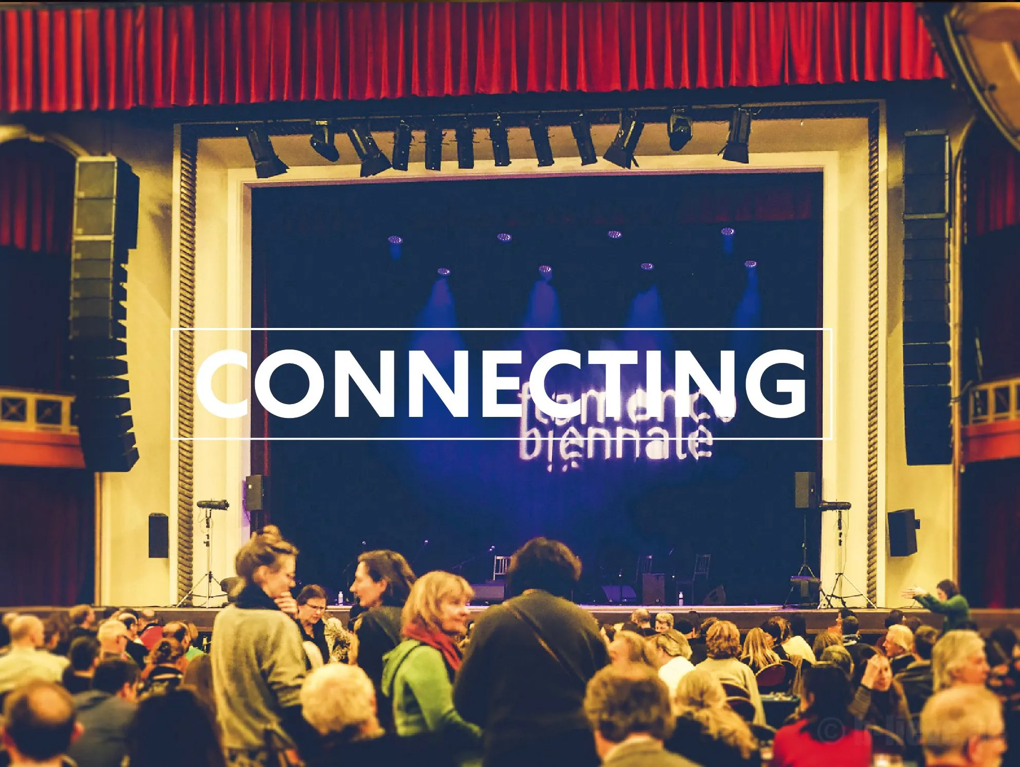 Audience facing a lit theatre stage with the Flamenco Biënnale logo and the word Connecting