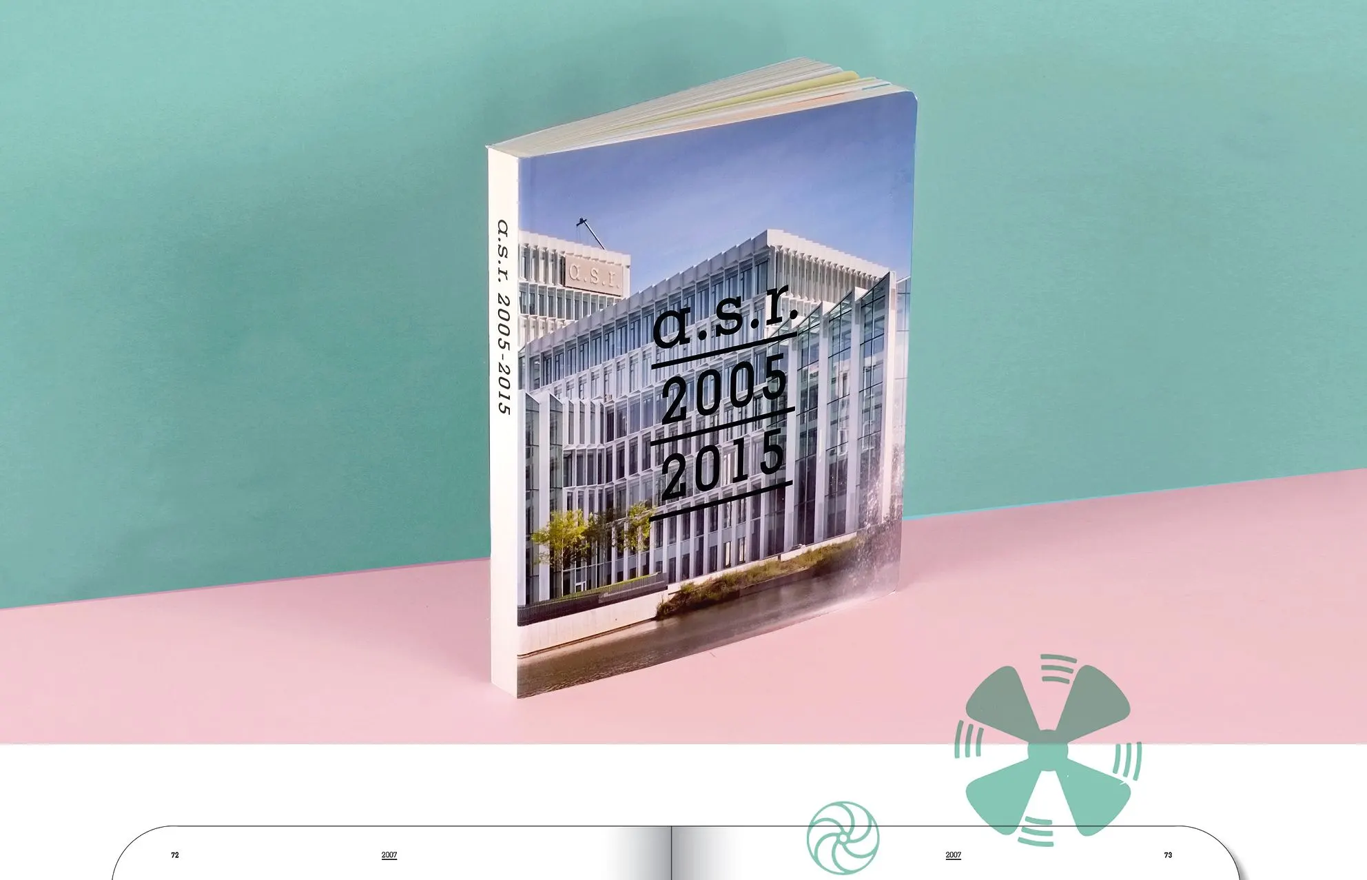Paperback book standing against a teal and pink background, titled a.s.r. 2005 2015, with a glass building on the cover