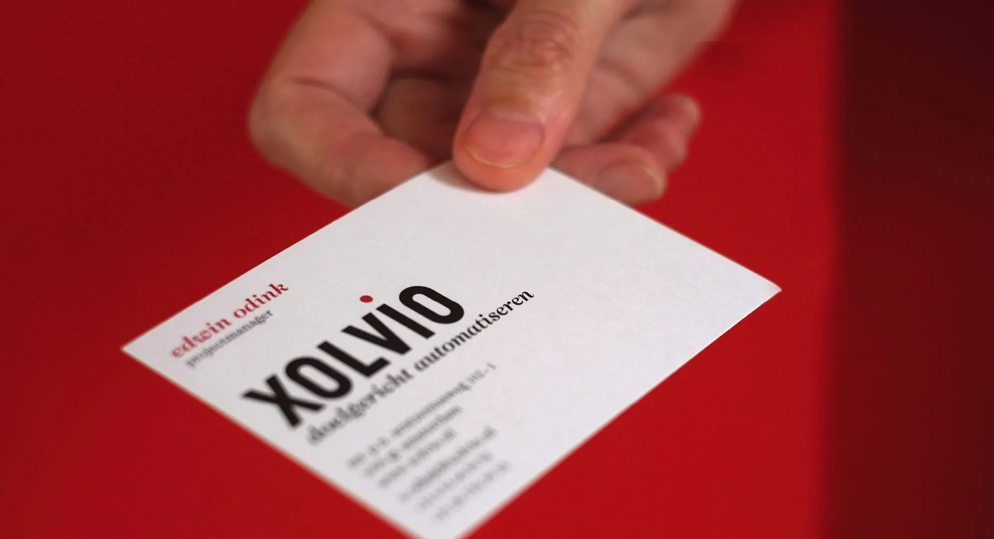 Business card held in a hand against a red background, showing the Xolvio logo and tagline