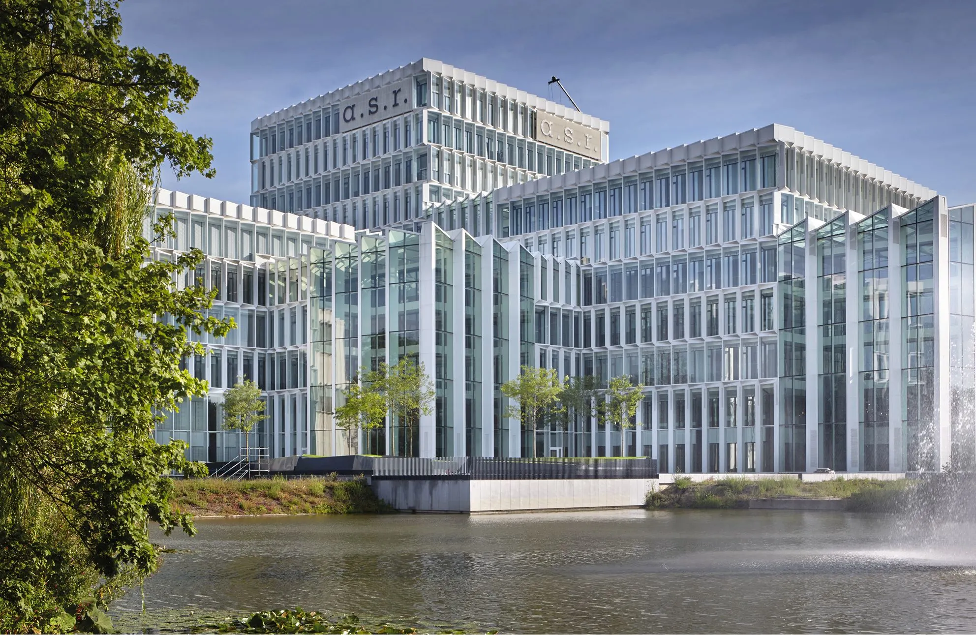 Modern glass office building of a.s.r. beside a pond with a fountain and trees