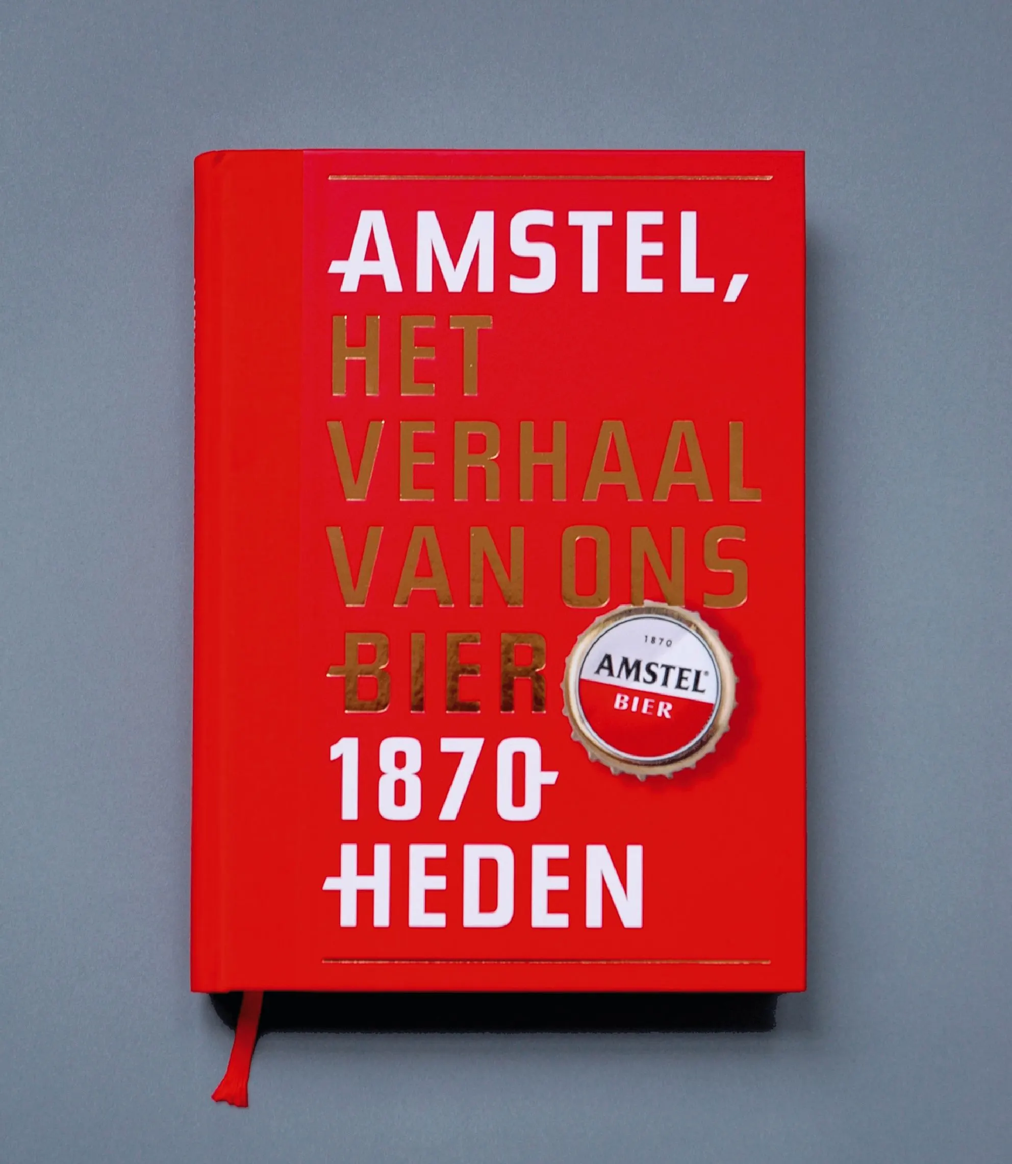 Red cover of the Amstel anniversary book 'Amstel, het verhaal van ons bier 1870-heden' with a bottle-cap emblem
