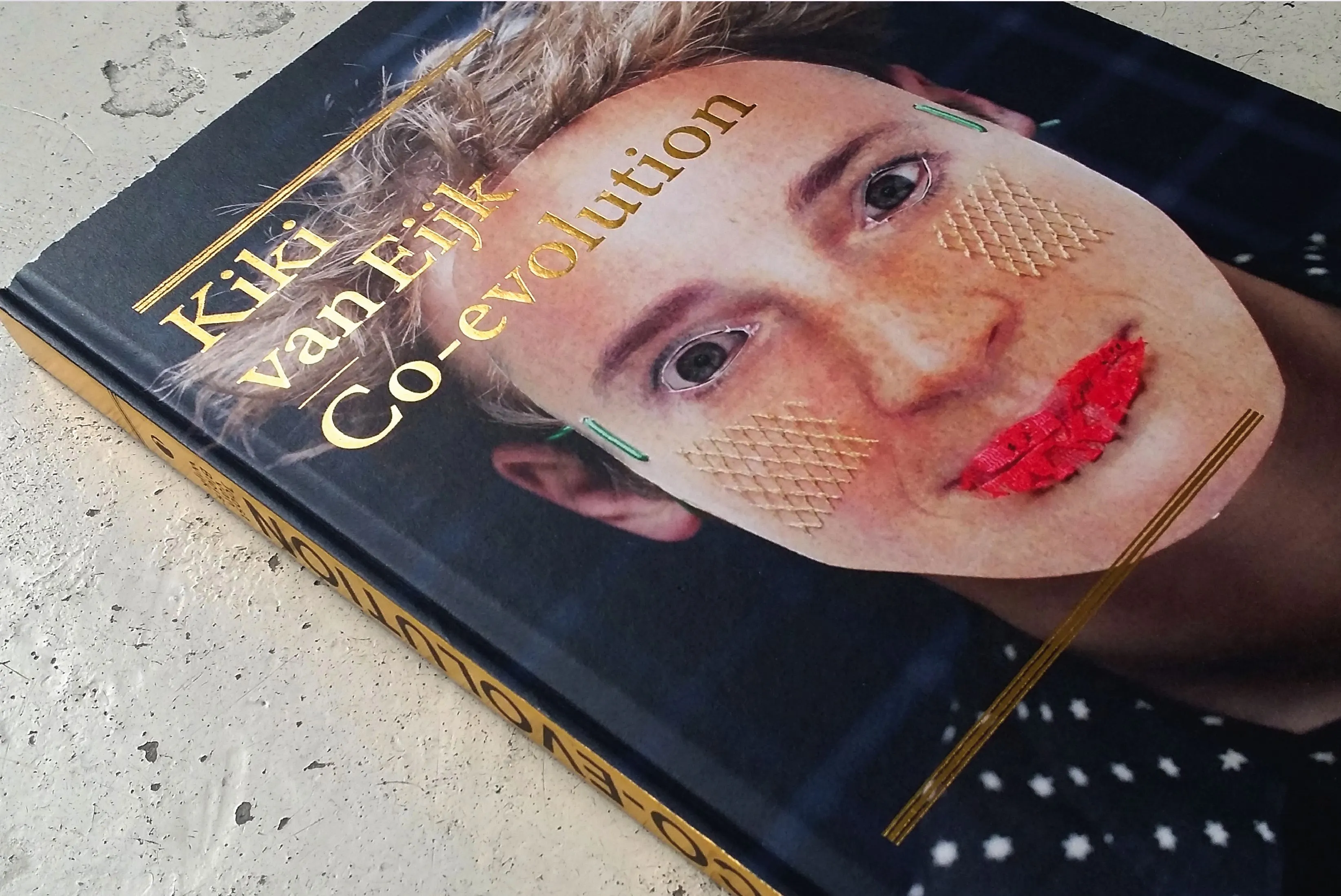 Cover of the Kiki van Eijk Co-evolution book with a face portrait, gold lettering and red lips