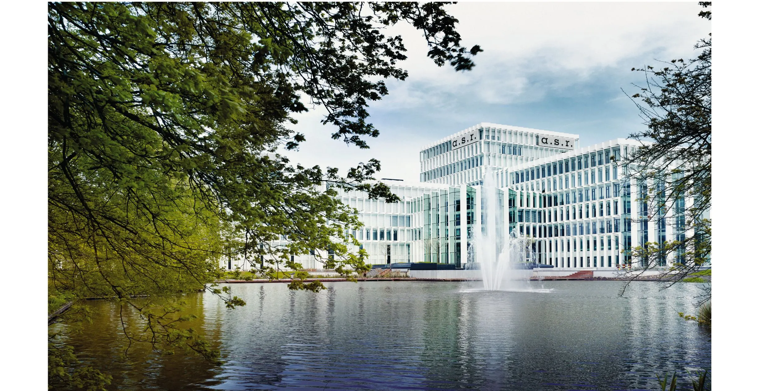 Photo of the white a.s.r. office building behind a pond with a fountain and trees
